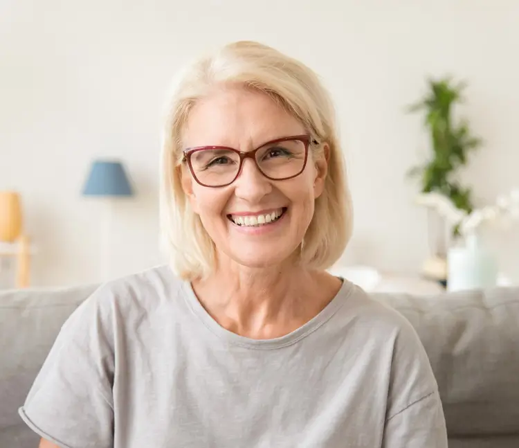 Porträt einer lächelnden Frau mit Brille in einem grauen T-Shirt auf einer Couch