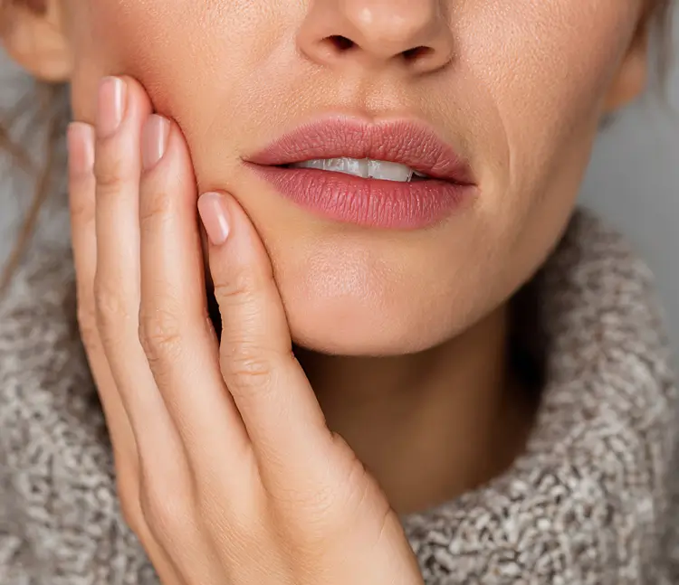 „Nahaufnahme des unteren Gesichts einer Frau. Sie legt ihre Hand an die Wange, die Lippen sind leicht geöffnet und die Zähne sichtbar.