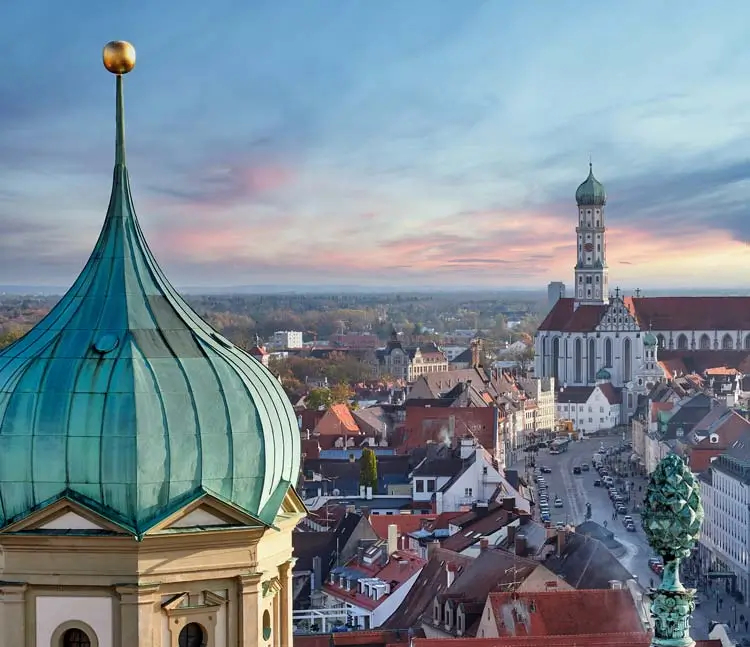 Stadtansicht Augsburg von oben. Im Vordergrund ist eine Kuppel mit gr&uuml;nem Dach zu sehen, im Hintergrund eine gro&szlig;e Kirche mit Turm