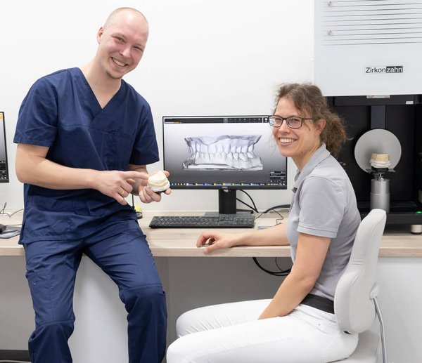 Chirurg und Zahntechniker besprechen gemeinsam einen Fall anhand eines 3D-Modells und lächeln in die Kamera