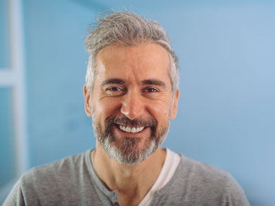 Grauhaariger Mann vor blauem Hintergrund lächelt in kamera