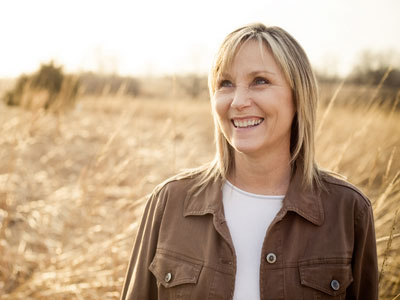 Frau in braunem Hemd steht auf einer Wiese und lächelt