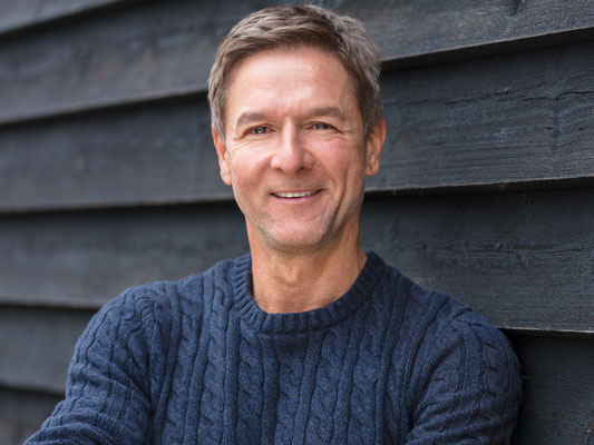 Mann mit Wollpulli vor dunklem Bretterhintergrund